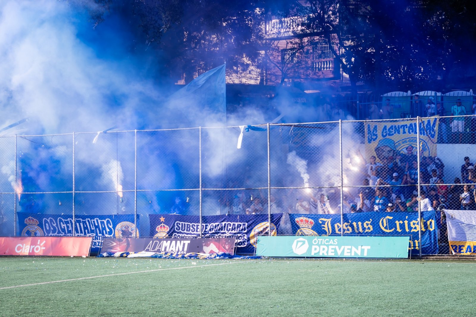 Torcida com fumaça azul e presença de marcas na beira do campo