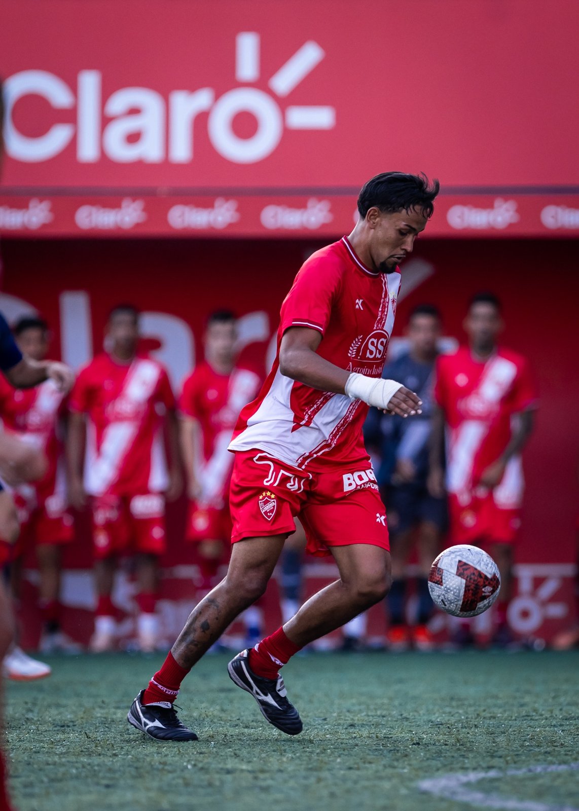 Atleta de uniforme vermelho em jogo com a marca Claro ao fundo